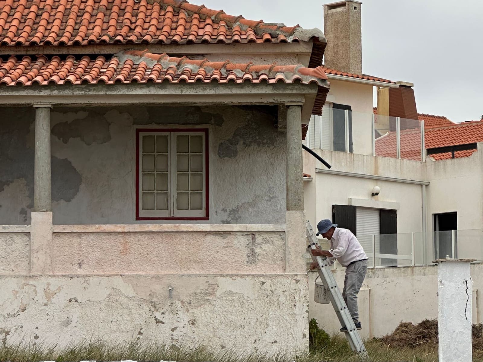 Façadier sur une échelle rénovant l'enduit d'une maison aux tuiles canal